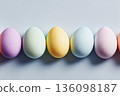 Brightly colored eggs in pastel shades are placed in a straight line on a soft surface. These eggs are commonly used during Easter for decoration and festivities 136098187