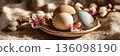 Easter eggs in different colors are arranged in a wooden bowl. Nearby, white flowers add a touch of spring. The setting has a soft, natural vibe, perfect for the holiday, banner 136098190