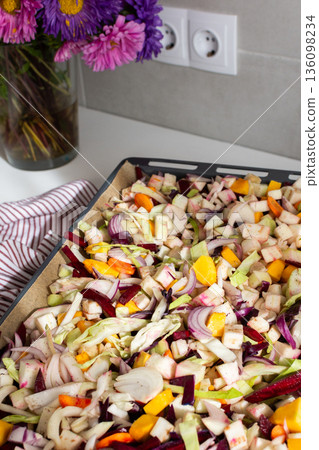 Fresh vegetables are chopped and placed on a baking tray ready for cooking in the oven. Colorful ingredients are showcased, and the setting is a welcoming kitchen Fresh vegetables are chopped and placed on a baking tray ready for cooking in the oven. Colorful ingredients are showcased, and the setting is a welcoming kitchen 136098234