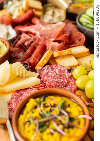 A colorful charcuterie board offers an inviting selection of cheeses, cured meats, fresh bread, nuts, and creamy hummus, perfect for sharing at a casual gathering or picnic A colorful charcuterie board offers an inviting selection of cheeses, cured meats, fresh bread, nuts, and creamy hummus, perfect for sharing at a casual gathering or picnic 136098235