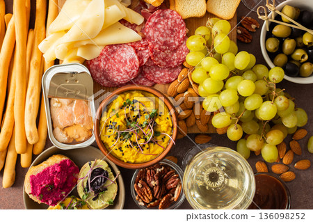 A colorful charcuterie board offers an inviting selection of cheeses, cured meats, fresh bread, nuts, and creamy hummus, perfect for sharing at a casual gathering or picnic A colorful charcuterie board offers an inviting selection of cheeses, cured meats, fresh bread, nuts, and creamy hummus, perfect for sharing at a casual gathering or picnic 136098252