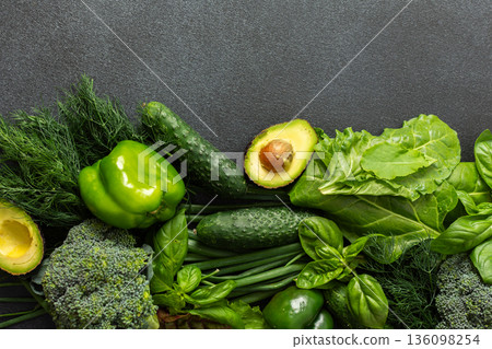 A vibrant assortment of fresh green vegetables is carefully arranged on a dark surface. 136098254