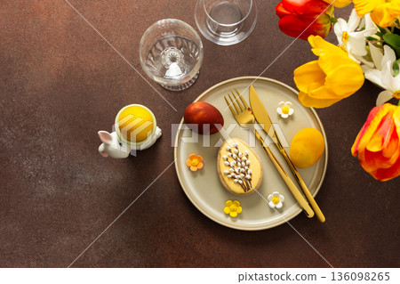 A beautifully arranged Easter table displays vibrant eggs, elegant gold cutlery, and a lively bouquet of tulips and lilies. This setting creates a cheerful atmosphere for the holiday feast A beautifully arranged Easter table displays vibrant eggs, elegant gold cutlery, and a lively bouquet of tulips and lilies. This setting creates a cheerful atmosphere for the holiday feast 136098265