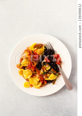 This wholesome breakfast includes black rice with stewed vegetables, stewed tomatoes, zucchini, peppers and onions top view 136098612