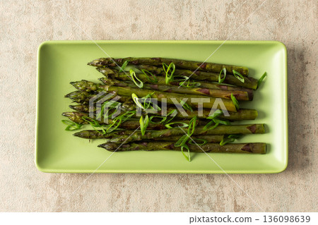 Asparagus spears are arranged neatly on a green plate, garnished with sliced green onions. This dish represents a simple yet flavorful vegetable choice for any meal 136098639