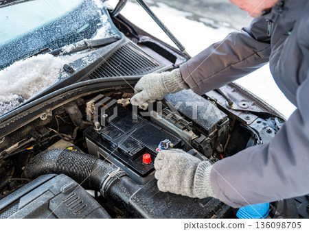 Man replacing car battery in winter cold with open hood during roadside emergency repair, emergency vehicle maintenance concept 136098705