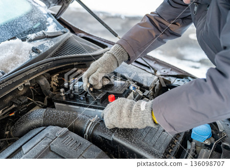 Man replacing car battery in winter cold with open hood during roadside emergency repair, emergency vehicle maintenance concept Man replacing car battery in winter cold with open hood during roadside emergency repair, emergency vehicle maintenance concept 136098707