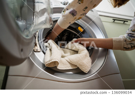 Washing machine at home. Smart appliances. Woman loading the washing machine with towels. Daily chores. Cleaning laundry Washing machine at home. Smart appliances. Woman loading the washing machine with towels. Daily chores. Cleaning laundry 136099034