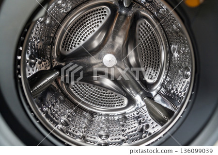 Stainless steel washing machine drum interior with perforated metal texture. Household appliance detail showing modern technology. Smart home appliances. Stainless steel washing machine drum interior with perforated metal texture. Household appliance detail showing modern technology. Smart home appliances. 136099039
