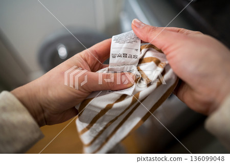 Woman reading clothing label with care symbols and information on clothing near washing machine, closeup 136099048