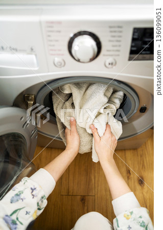 Washing machine at home. Smart appliances. Woman loading the washing machine with towels. Daily chores. Cleaning laundry Washing machine at home. Smart appliances. Woman loading the washing machine with towels. Daily chores. Cleaning laundry 136099051