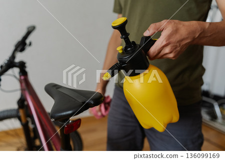 Close-up of bicycle mechanic spraying water on bicycle saddle performing detailed maintenance and cleaning in workshop environment, ensuring optimal hygiene and care. Concept of bike service. Close-up of bicycle mechanic spraying water on bicycle saddle performing detailed maintenance and cleaning in workshop environment, ensuring optimal hygiene and care. Concept of bike service. 136099169
