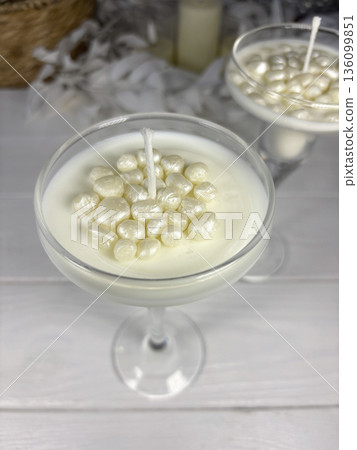 White candles in a glass candle holder. Wax pearls near the wick. The candles are standing on white boards. 136099851