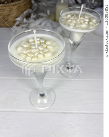 White candles in a glass candle holder. Wax pearls near the wick. The candles are standing on white boards. 136099853