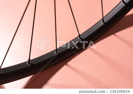 Black bicycle rim with thin metal spokes casting shadows on a matte pink background. Black bicycle rim with thin metal spokes casting shadows on a matte pink background. 136100634