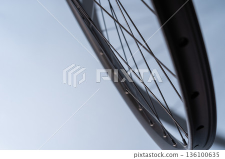 Close-up of a black bicycle rim with spokes against a smooth light blue background. 136100635