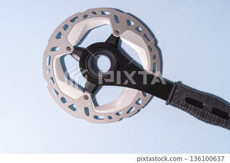 Close-up of a metallic bicycle disc brake rotor attached to a black handle on a blue background Close-up of a metallic bicycle disc brake rotor attached to a black handle on a blue background 136100637