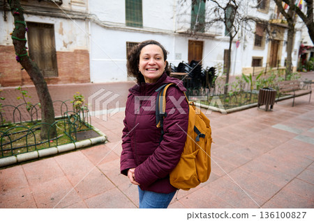 Smiling Woman With Maroon Jacket And Orange Backpack On Urban Street Scene Smiling Woman With Maroon Jacket And Orange Backpack On Urban Street Scene 136100827