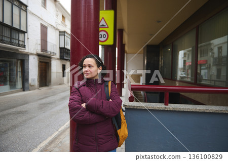 Woman in Burgundy Winter Coat Standing on City Street Near Red Pillar and Signage Outdoor Woman in Burgundy Winter Coat Standing on City Street Near Red Pillar and Signage Outdoor 136100829