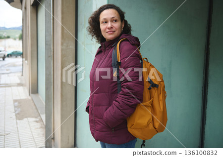 Woman With Burgundy Jacket And Orange Backpack Standing On City Street Woman With Burgundy Jacket And Orange Backpack Standing On City Street 136100832