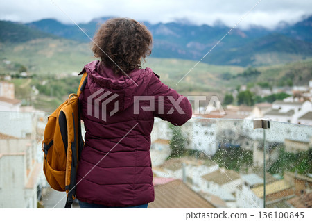 Woman With Orange Backpack Standing On Balcony Overlooking Mountain Village View 136100845