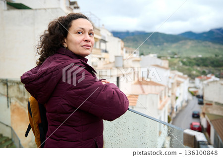 Thoughtful Woman Standing On Balcony In Burgundy Jacket Overlooking Scenic Town And Hills Thoughtful Woman Standing On Balcony In Burgundy Jacket Overlooking Scenic Town And Hills 136100848