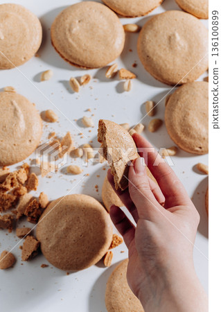 Hand holding bitten peanut macaron on white background with crumbs and nuts 136100899
