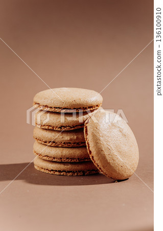 Beige macarons stacked on brown background, minimal French dessert Beige macarons stacked on brown background, minimal French dessert 136100910