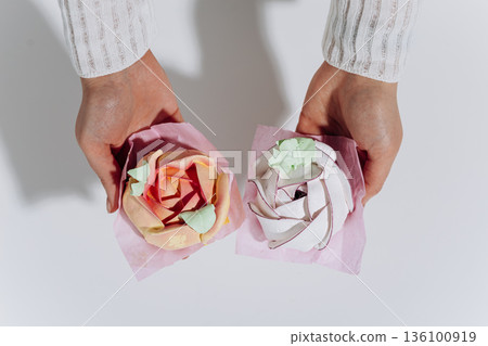 Hands holding pastel meringue swirls on pink paper, minimal white background Hands holding pastel meringue swirls on pink paper, minimal white background 136100919