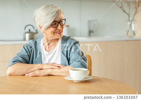 Good morning. Comfort relaxed senior old elderly woman grandmother drinking hot beverage tea coffee in kitchen at home. Mature woman resting enjoy calm morning at modern home alone. Pension concept 136101087
