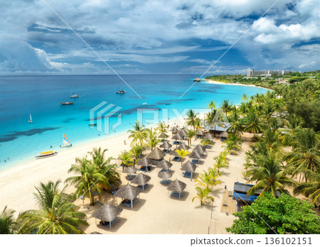 Aerial view of sandy beach, palm trees, umbrellas, boats, sea Aerial view of sandy beach, palm trees, umbrellas, boats, sea 136102151