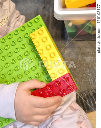 A toddler builds a house from bright construction sets on a green platform. A toddler builds a house from bright construction sets on a green platform. 136102177