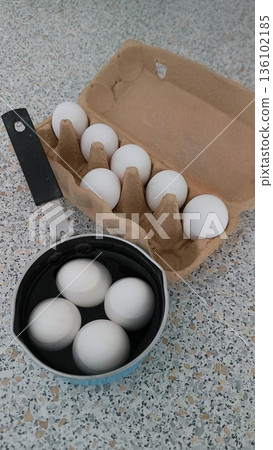 Preparing to boil eggs. White chicken eggs in a saucepan with water and a cardboard tray. 136102185