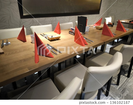 A restaurant interior with a long table set and red napkins A restaurant interior with a long table set and red napkins 136102187