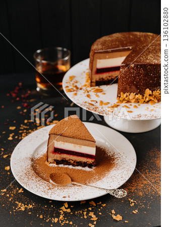 Chocolate mousse cake slice with berry layer on plate, cocoa dust, dark backdrop 136102880