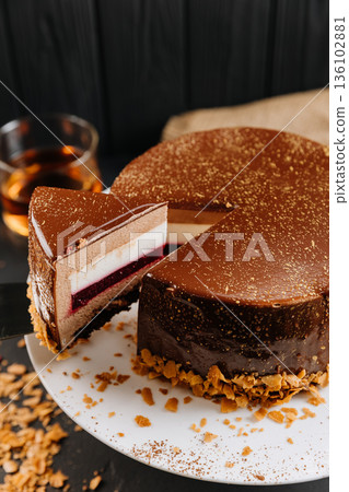 Layered chocolate mousse cake slice with raspberry jelly on spatula, dark background Layered chocolate mousse cake slice with raspberry jelly on spatula, dark background 136102881