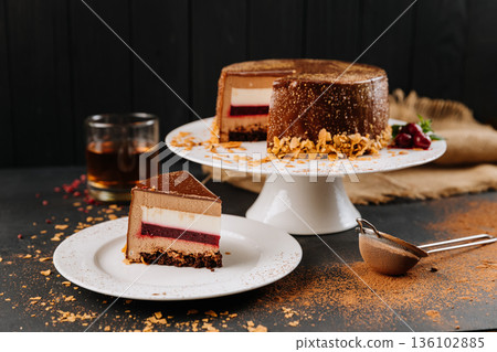 Chocolate mousse cake slice with berry layer on plate, cocoa dust, dark backdrop 136102885
