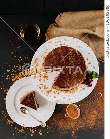 Chocolate mousse cake slice with berry layer on plate, cocoa dust, dark backdrop 136102886