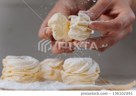 Hands breaking vanilla zephyr with powdered sugar, close-up homemade dessert 136102891