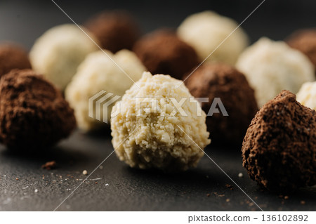 Macro coconut truffle with creamy center and cocoa truffles on dark slate Macro coconut truffle with creamy center and cocoa truffles on dark slate 136102892