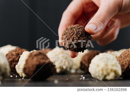 Hand picking cocoa truffle candy on dark background, macro closeup 136102896