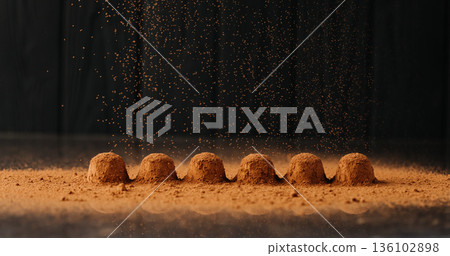 Cocoa powder falling over chocolate truffles with reflection on black background Cocoa powder falling over chocolate truffles with reflection on black background 136102898