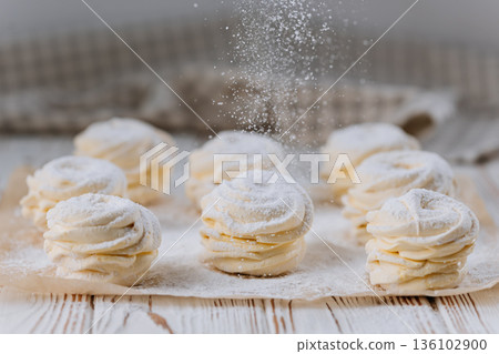Powdered sugar falling on vanilla zephyr rosettes on parchment, rustic background 136102900