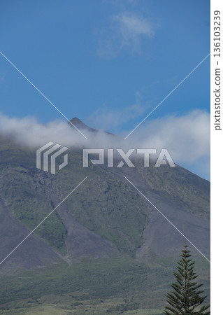 Low clouds drift across the slopes of Mount Pico on Pico Island, with green volcanic terrain and clear blue sky above Low clouds drift across the slopes of Mount Pico on Pico Island, with green volcanic terrain and clear blue sky above 136103239