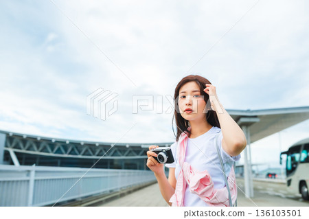 A woman holding a camera at a bus stop. Photo courtesy of Kansai International Airport (KIX). 136103501