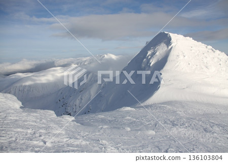 A mountain covered in snow with a cloudy sky in the background A mountain covered in snow with a cloudy sky in the background 136103804
