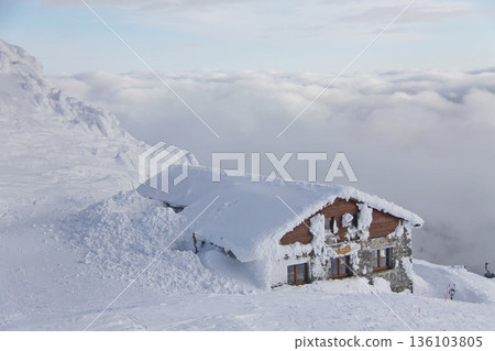 Snow-covered alpine mountain hut nestled on a high ridge. 136103805