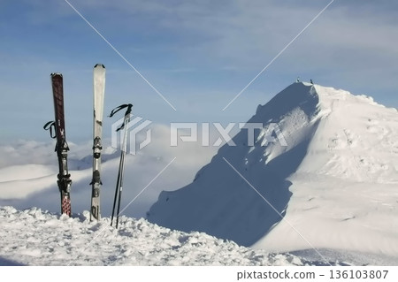 A pair of skis and poles stuck in the snow and a sharp, snowy ridge A pair of skis and poles stuck in the snow and a sharp, snowy ridge 136103807
