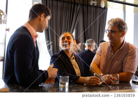 Business professionals talking and smiling together at a modern office counter during a networking break, holding glasses of water, representing teamwork, trust, collaboration, and positive corporate Business professionals talking and smiling together at a modern office counter during a networking break, holding glasses of water, representing teamwork, trust, collaboration, and positive corporate 136103859