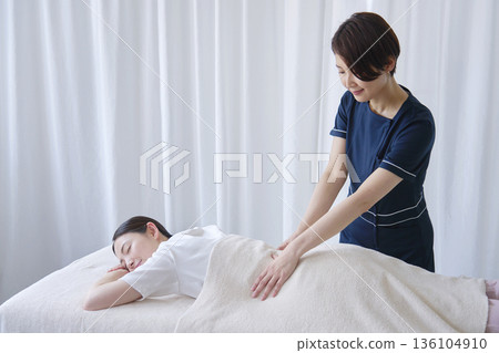 Female masseuse doing a back massage Female masseuse doing a back massage 136104910